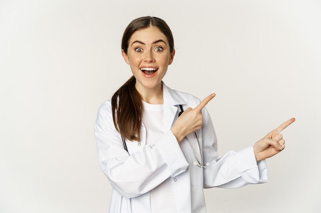 Ärztin ärztin in medizinischer uniform zeigt mit dem finger nach rechts und zeigt bannerwerbung lächelnd ...