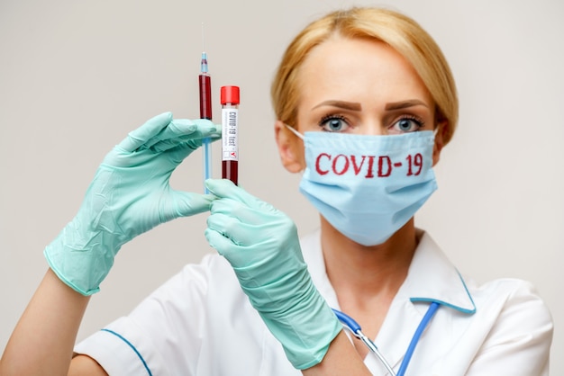 Ärztin der Krankenschwester, die Schutzmaske und Handschuhe trägt, die Virusblut-Reagenzglas und Spritze halten