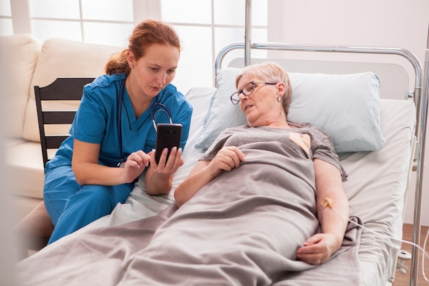 Ärztin, die älterer frau im pflegeheim hilft, ihr telefon zu benutzen.