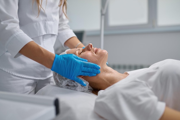 Foto Ärztin, kosmetikerin, die zur hautpflege eine maske auf das gesicht des patienten aufträgt. kosmetisches verfahren zur hautpflege, verjüngung und ernährung