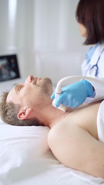 Ärztin mit blauen medizinischen Handschuhen führt eine Ultraschalluntersuchung des Halses bei einem männlichen Patienten durch