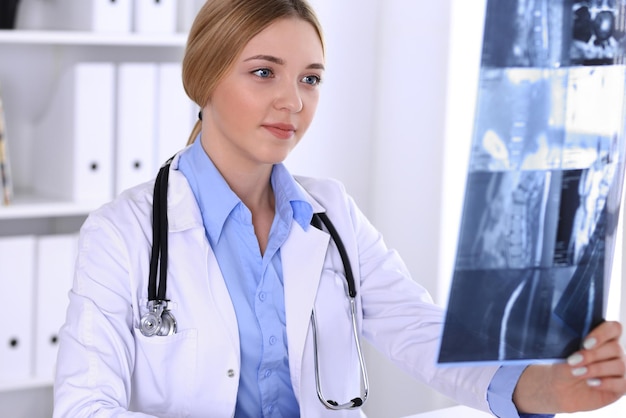 Ärztin untersucht Röntgenbild in Fensternähe im Krankenhaus. Chirurg oder Orthopäde bei der Arbeit. Medizin- und Gesundheitskonzept. Blau gefärbte Bluse eines Therapeuten sieht gut aus.