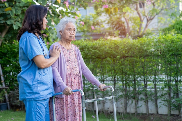 Ärztliche Hilfe und Pflege Asiatische Senioren oder ältere alte Damen benutzen Walker mit starker Gesundheit, während sie im Park in fröhlichen, frischen Ferien spazieren gehen