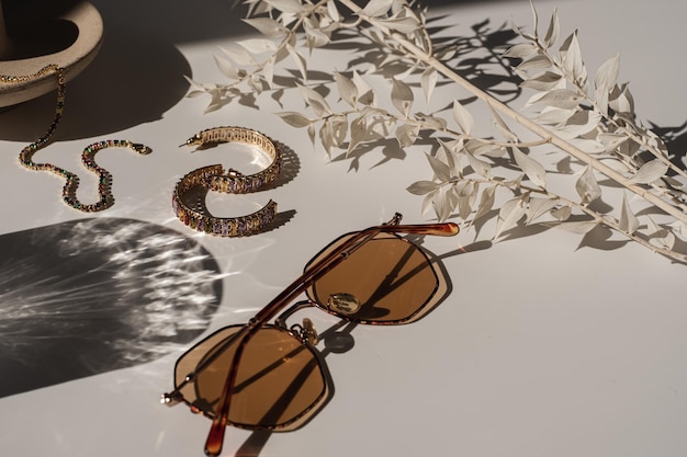 Ästhetische Luxus-Mode-Boutique-Branding-Komposition Eleganter böhmischer Glamour weiblicher Schmuck und Accessoires mit Sonnenlicht-Schatten Sonnenbrillen-Ohrring-Armband-Pflanze