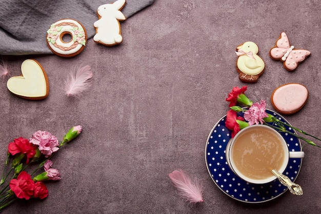 Ästhetische Osterkaffeezeit Verglaste Kekse Kaffeetasse Federn Asterblumen flach lag Stilvoller Frühlingshintergrund mit Kopierraum