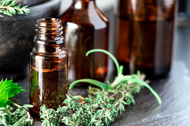 Foto Ätherische öle in einer braunen glasflasche, thymian, rosmarin und minze auf dem tisch. ätherisches kräuteröl, aromatherapie. kategorie lebensstil