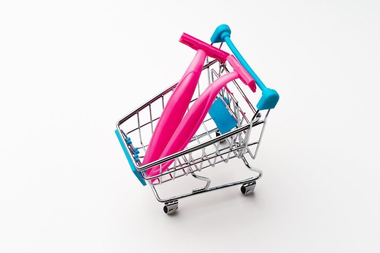 Foto afeitadora desechable femenina en carrito de compras de juguete sobre fondo blanco cerrar