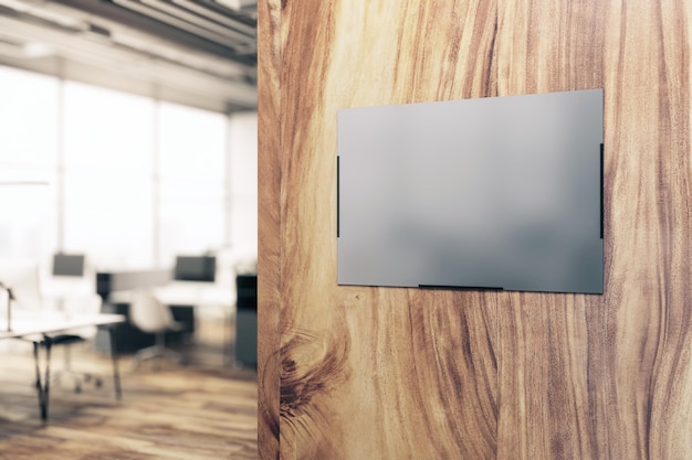 Afiche gris en blanco con reflejo y espacio para su logo o texto publicitario sobre fondo de pared de madera natural en un área de oficina moderna con muebles borrosos en la maqueta de representación 3D de fondo