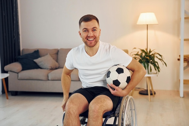 Aficionado al fútbol con balón Hombre discapacitado en silla de ruedas está en casa