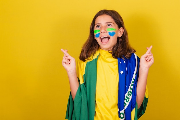 Aficionado al fútbol infantil caucásico brasileño con los dedos cruzados vitoreando deseando esperanzados Juegos Olímpicos de la Copa del Mundo