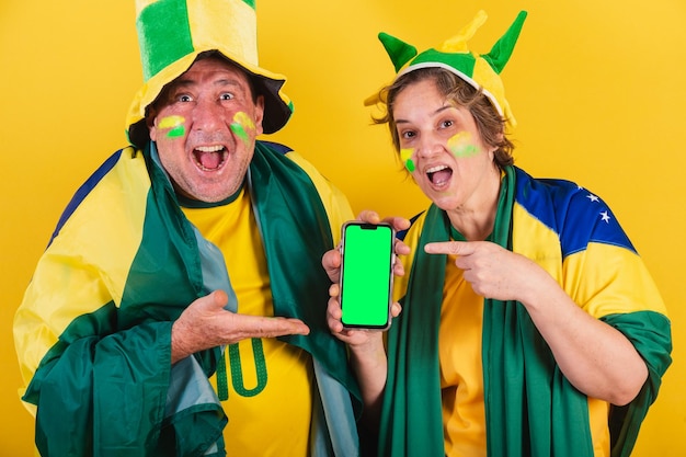 Aficionado al fútbol de pareja adulta de brasil con bandera apuntando a la aplicación de pantalla de teléfono inteligente foto de publicidad móvil