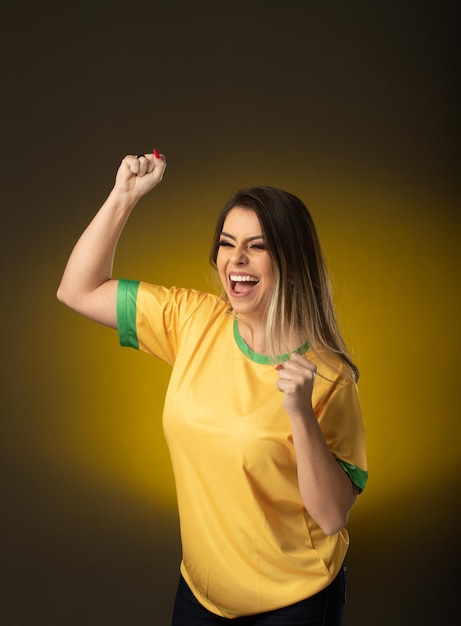 Aficionado brasileño Aficionado a la mujer brasileña celebrando en fútbol o partido de fútbol sobre fondo amarillo Colores de Brasil