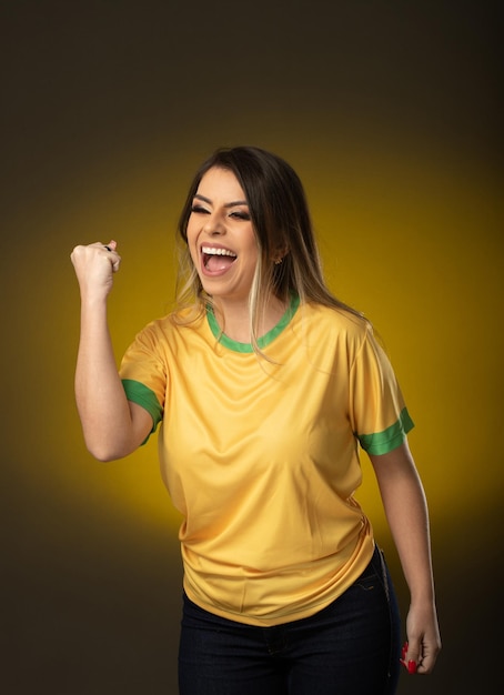 Aficionado brasileño Aficionado a la mujer brasileña celebrando en fútbol o partido de fútbol sobre fondo amarillo Colores de Brasil