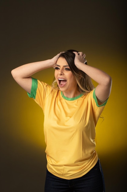 Aficionado brasileño Aficionado a la mujer brasileña celebrando en fútbol o partido de fútbol sobre fondo amarillo Colores de Brasil