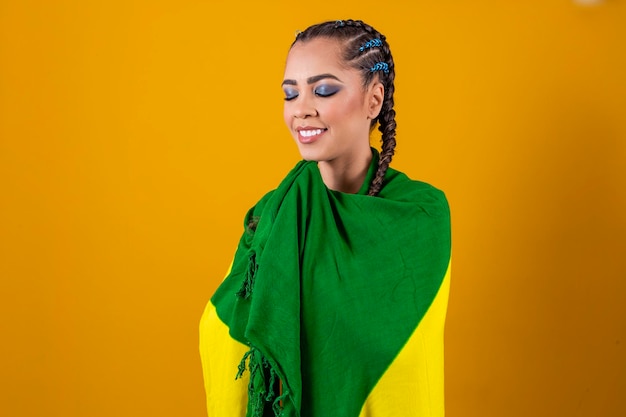 Aficionado brasileño sosteniendo la bandera de Brasil sobre fondo gris Joven mujer brasileña sonriente sonriendo a la cámara con la bandera de Brasil