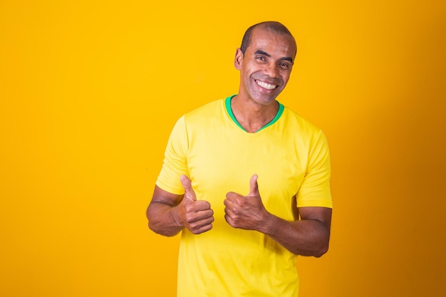 Aficionado a los deportes brasileño apoyando a su equipo nacional animando con los brazos extendidos y pulgares hacia arriba con la camiseta