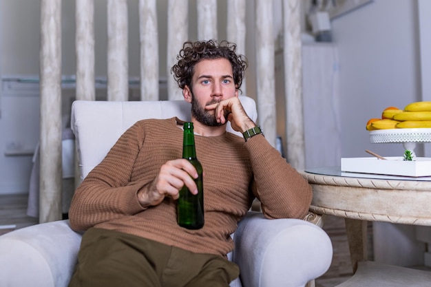 Aficionado a los deportes triste sentado en un sofá y viendo un partido en la televisión con su equipo perdiendo el juego. Hombre viendo fútbol o partido de fútbol en la televisión en casa y bebiendo cerveza