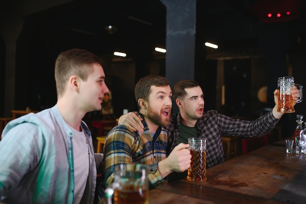 Aficionados al fútbol en el bar Aficionados al fútbol felices animando en el bar y bebiendo cerveza mientras el camarero sirve cerveza en el fondo