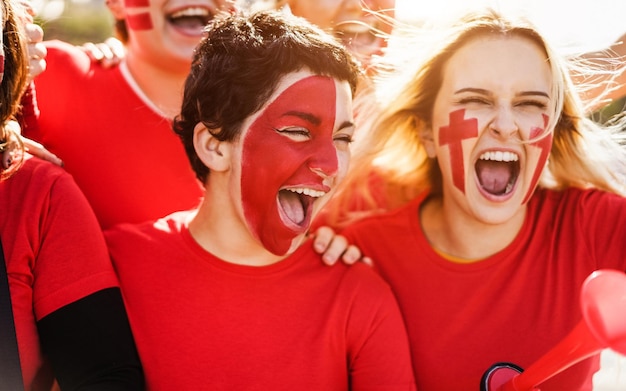 Los aficionados al fútbol deportivo rojo gritan mientras apoyan a su equipo fuera del estadio. Centrarse en la cara de la chica central.