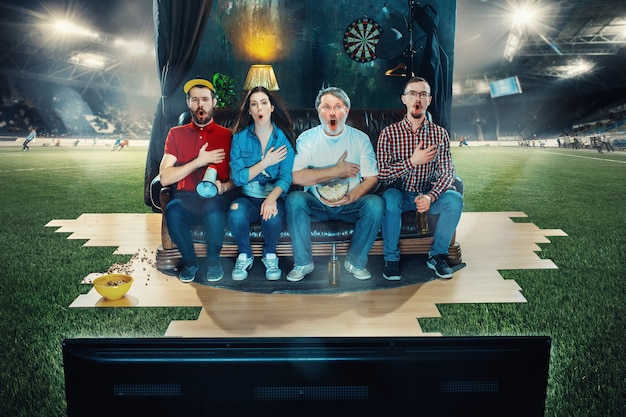 Foto aficionados al fútbol fútbol sentado en el sofá y viendo la televisión en medio de un campo de fútbol