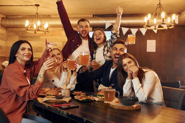 Aficionados al fútbol Grupo de jóvenes amigos sentados juntos en el bar con cerveza