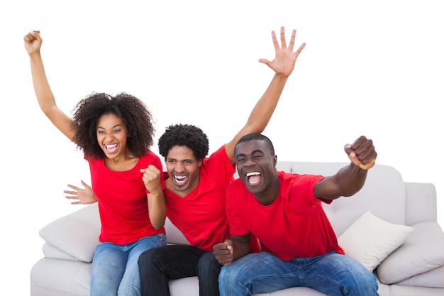 Aficionados al fútbol en rojo animando en el sofá