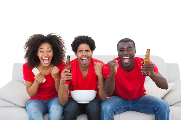 Aficionados al fútbol en rojo animando en el sofá