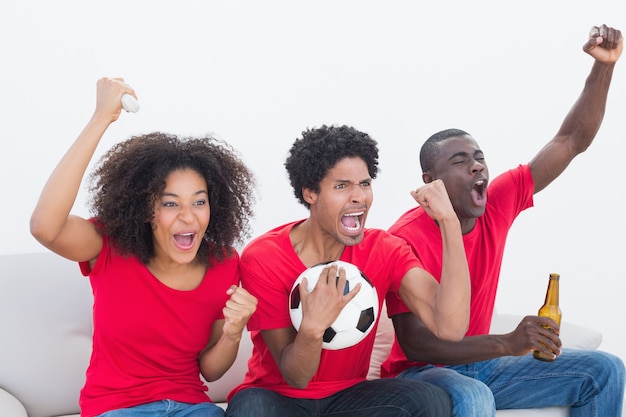 Aficionados al fútbol en rojo sentado en el sofá animando