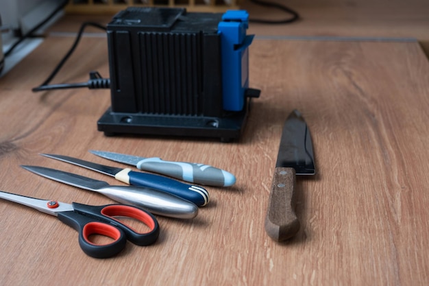 Afilar un cuchillo en un afilador eléctrico en casa Flatlay hoja de cuchillo tijeras afiladores polvo vuela en la máquina