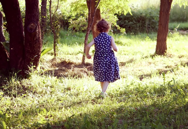 Aforable kleines Mädchen mit lockigem Haar, das im Sommergarten auf dem Land spazieren geht