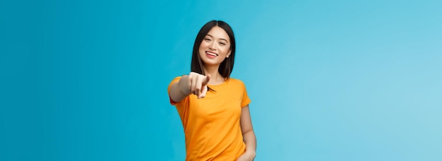 Afortunado ganador alegre carismático asiático linda chica urbana stand camiseta amarilla sonriendo amigable pointin