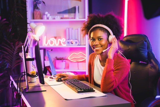 African American girl gaming streamer equipe vencedora jogando on-line lutando com Esport usando fones de ouvido em sala de iluminação de néon falando com outros jogadores planejando estratégias para vencer concorrentes Tastemaker