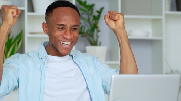 AfricanAmerican se siente feliz de recibir una gran noticia por Internet mira la pantalla de la PC, manos levantadas gritan de alegría celebrando la victoria de la lotería en línea