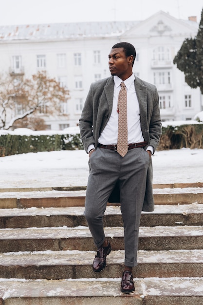 Africano - hombre de negocios estadounidense con teléfono inteligente en la calle de la ciudad de invierno cubierto de nieve