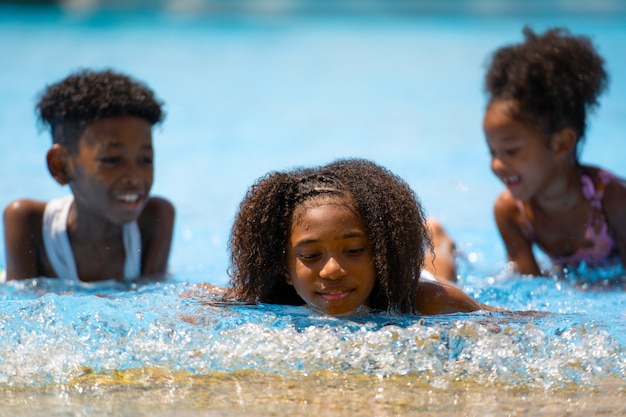 Africano menina e menino sentado e jogando água na piscina do parque de diversões.