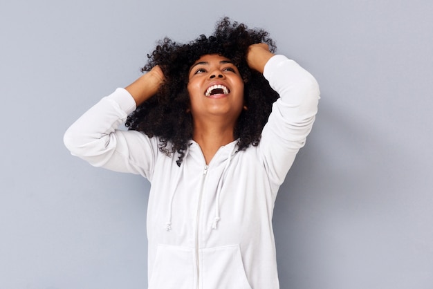 Afrikanerin, die mit den Händen im Haar auf grauem Hintergrund lächelt