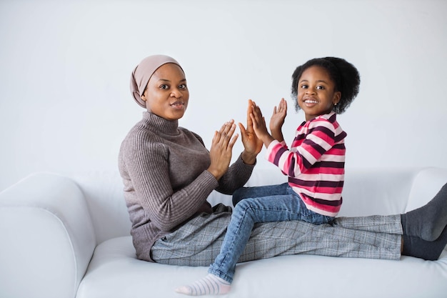 Afrikanerin im Hijab klatscht mit Töchtern auf der Couch in die Hände