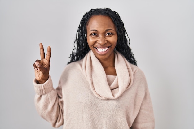 Afrikanerin steht vor weißem Hintergrund und zeigt mit den Fingern Nummer zwei nach oben, während sie selbstbewusst und glücklich lächelt