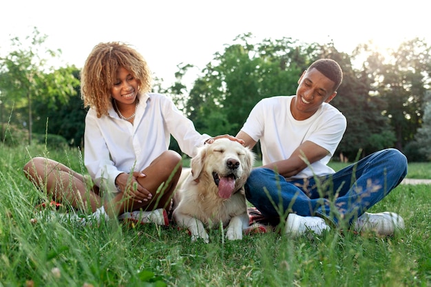 afrikanisch-amerikanisches glückliches Paar mit Hund sitzen im Sommer im Park und entspannen sich Mann und Frau