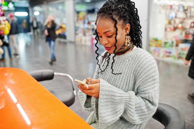 Afrikanische Bloggerin posierte in Pullover und Jeans mit ihrem Handy im Einkaufszentrum