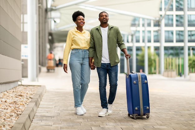 Afrikanische Ehepartner, die in den Urlaub reisen und mit Koffer am Flughafen spazieren gehen