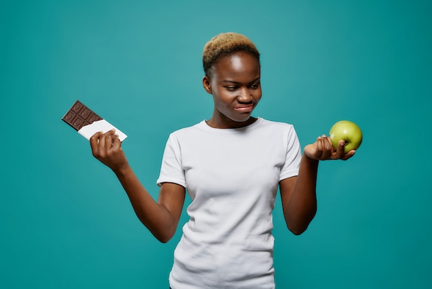 Afrikanische Frau, die schmackhafte Schokolade und gesunden Apfel hält