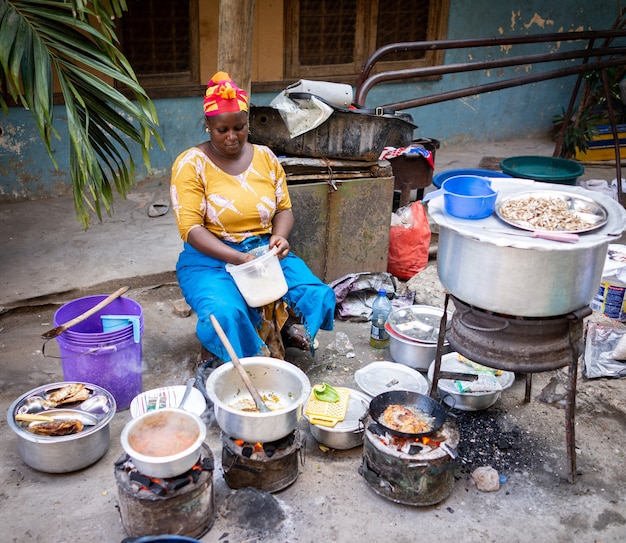 Afrikanische frau, die traditionelles essen auf der straße kocht