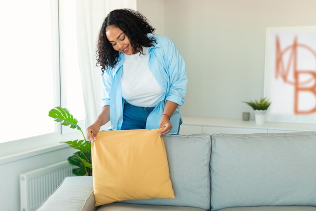Afrikanische Frau, die Zimmer dekoriert, die zu Hause Kissen auf die Couch legt