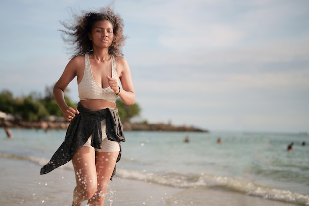 Afrikanische Frau im Sport-BH läuft am Strand für Outdoor-Training Portrait sexy asiatische afrikanische Dame bereitet sich auf Fitness am Strand vor