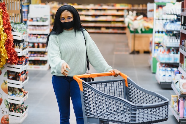 Afrikanische Frau mit medizinischer Einwegmaske. Einkaufen im Supermarkt während des Ausbruchs der Coronavirus-Pandemie. Epidemiezeit.