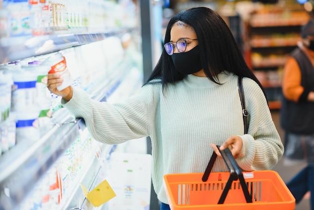 Afrikanische Frau mit medizinischer Einwegmaske. Einkaufen im Supermarkt während des Ausbruchs der Coronavirus-Pandemie. Epidemiezeit.
