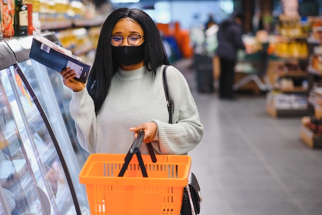 Afrikanische Frau mit medizinischer Einwegmaske. Einkaufen im Supermarkt während des Ausbruchs der Coronavirus-Pandemie. Epidemiezeit.