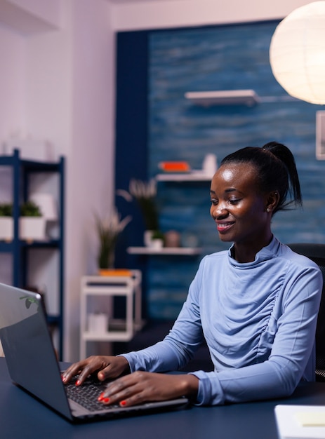 Afrikanische Geschäftsfrau, die am Laptop arbeitet und versucht, spät in der Nacht eine Frist für die Arbeit von zu Hause aus zu beenden. Schwarzer Unternehmer, der am persönlichen Arbeitsplatz sitzt und auf der Tastatur schreibt.