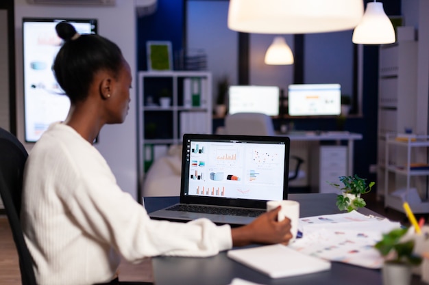 Afrikanische Geschäftsfrau, die spät nachts im Büro mit Finanzstatistiken arbeitet